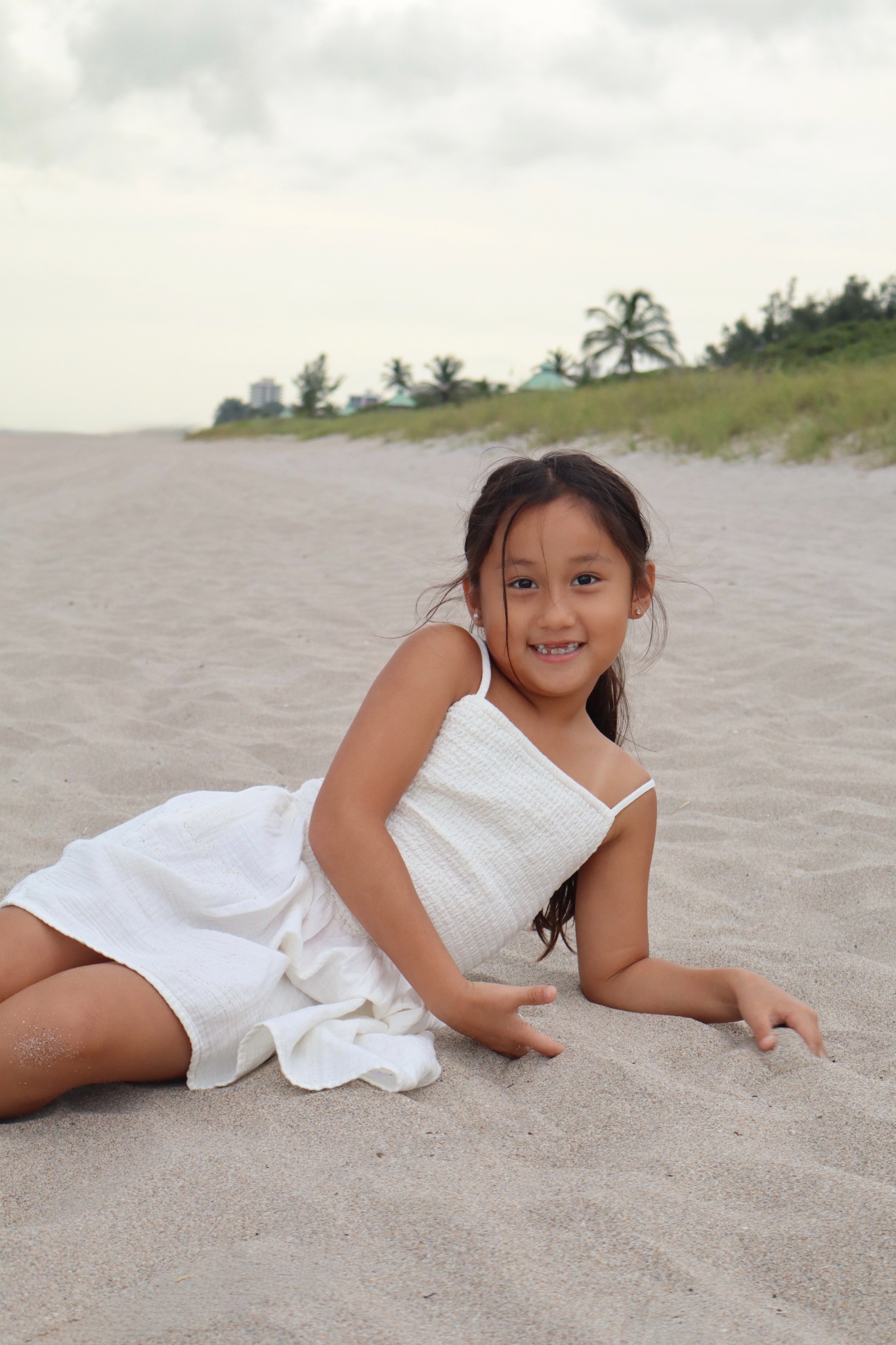 Young girl in a white dress sitting on a sandy beach